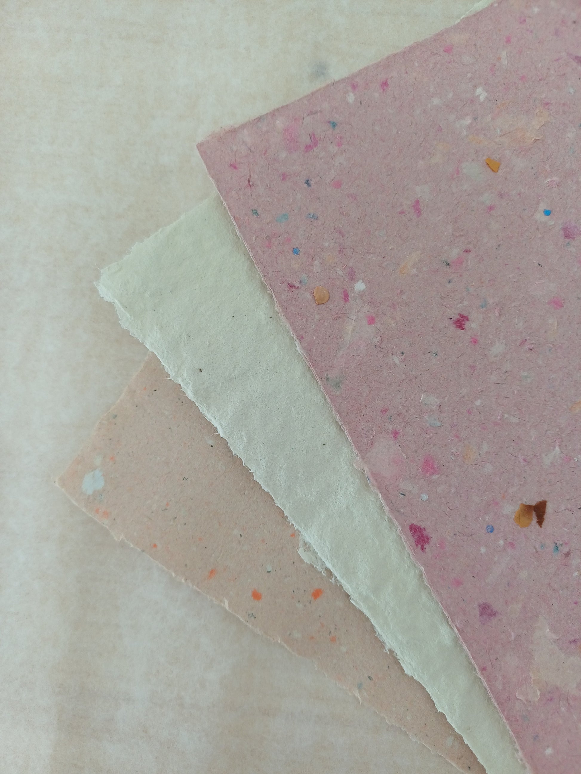 Coin de trois feuilles de papier recyclé maison, beige, blanche et rose.
