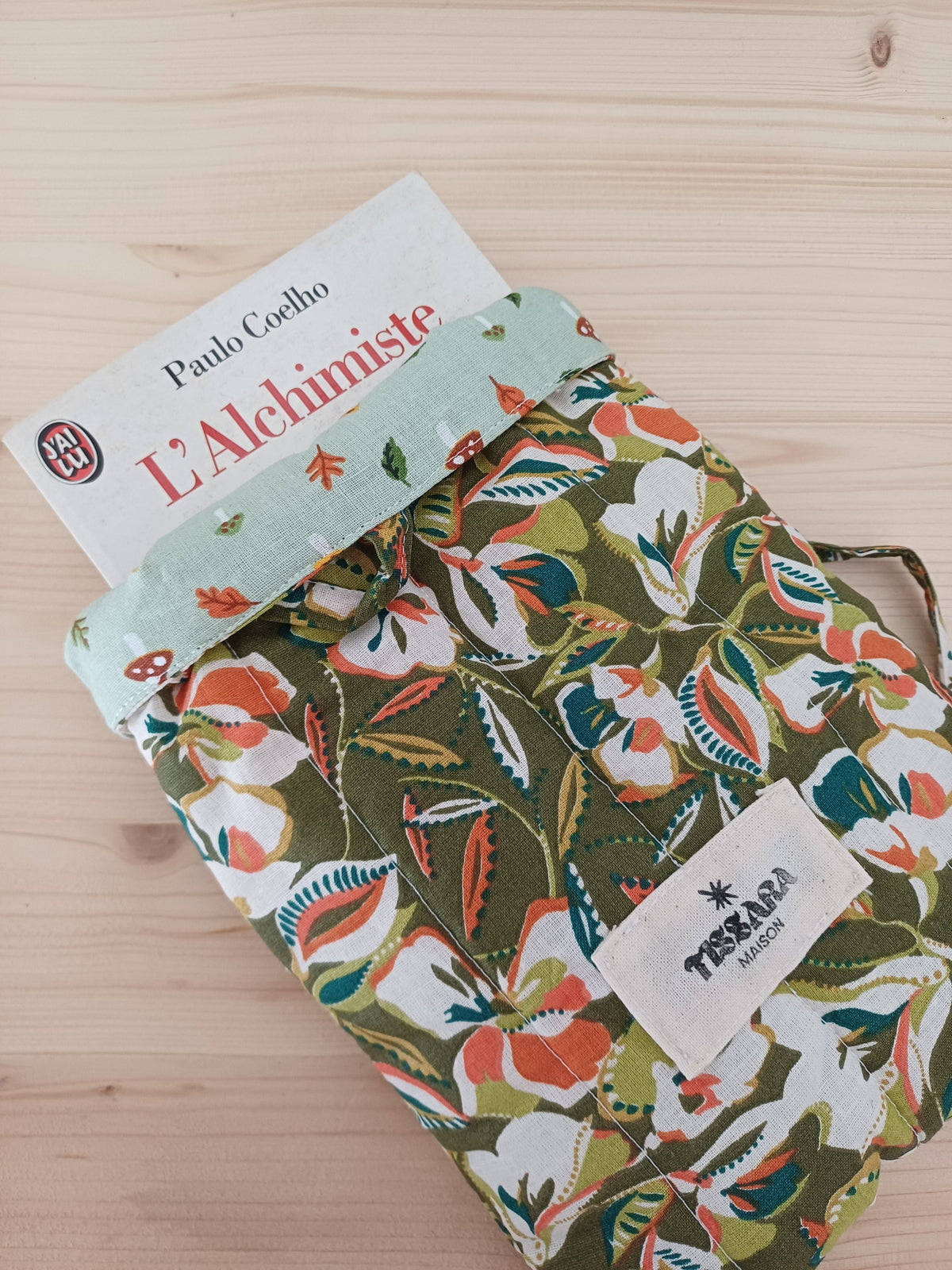 Pochette en tissu aux motifs floraux avec un ruban sur le sommet, les bords supérieurs sont retournés et dévoilent e haut d'un livre.